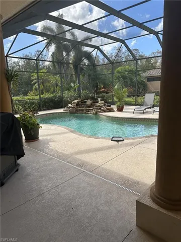 View of pool with pool water feature, glass enclosure, area for grilling, and a patio area