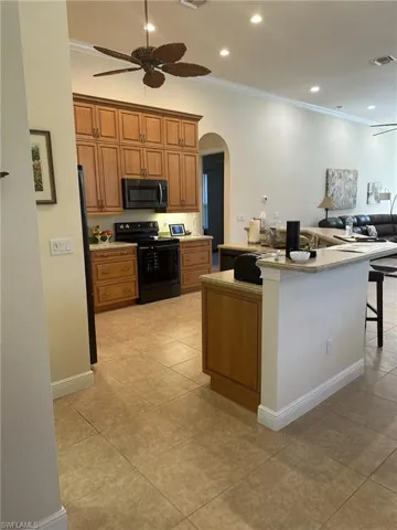 Kitchen featuring ornamental molding, black / electric stove, a breakfast bar area, and light tile patterned flooring