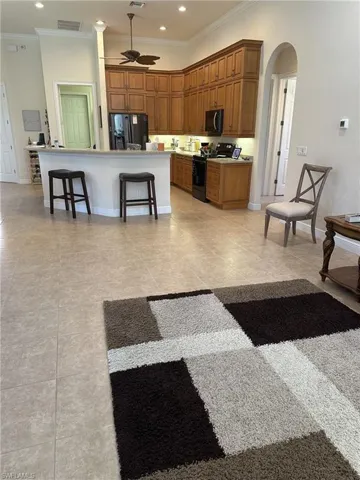 Kitchen with a center island, black appliances, ceiling fan, ornamental molding, and a breakfast bar area