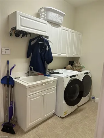Laundry room with cabinets, light tile patterned floors, washing machine and clothes dryer, and sink