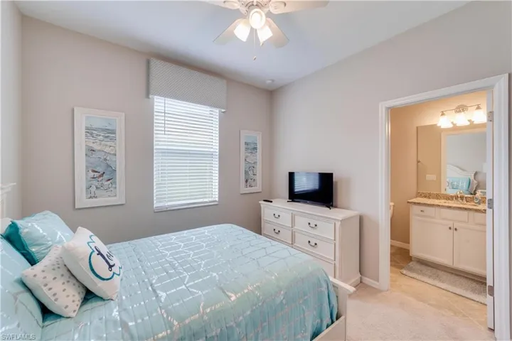 Second Bedroom with light colored carpet, light tile patterned flooring, ceiling fan, ensuite bathroom, and baseboards