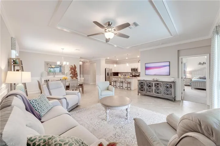 Living room with light tile patterned flooring, ceiling fan with notable chandelier, a raised ceiling, and crown molding