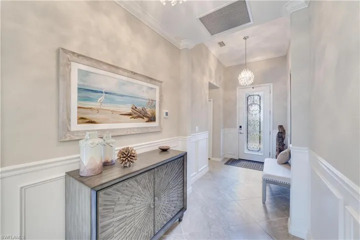 Foyer with ornamental molding, wainscoting, and an beautiful chandelier
