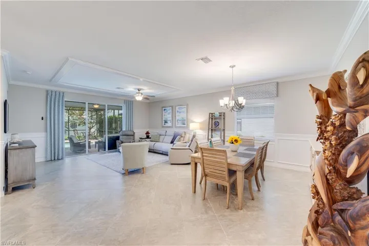 Dining room open to living room and kitchen with wainscoted walls, ornamental molding and ceiling fan with notable chandelier. Large open concept living.