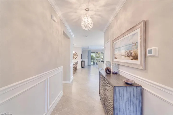 Hallway with a chandelier, a wainscoted wall, crown molding, and a decorative wall