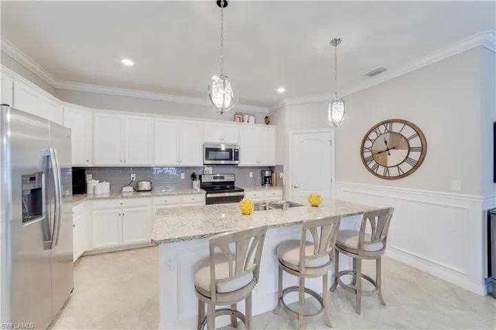 Kitchen with an island with sink, white cabinetry, granite counters,  stainless steel appliances, and decorative light fixtures