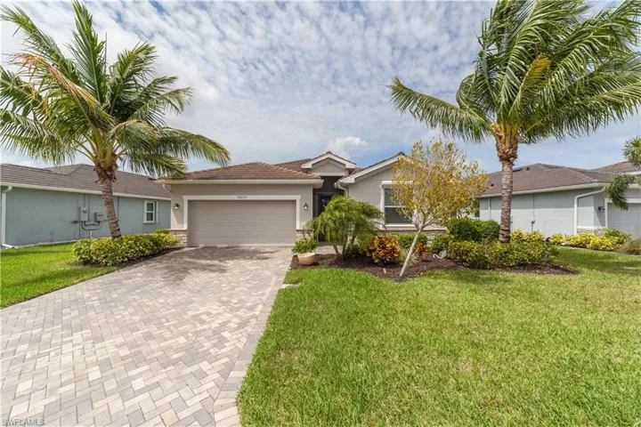 Single story home featuring a garage, a tile roof, decorative driveway, a front lawn, and stucco siding