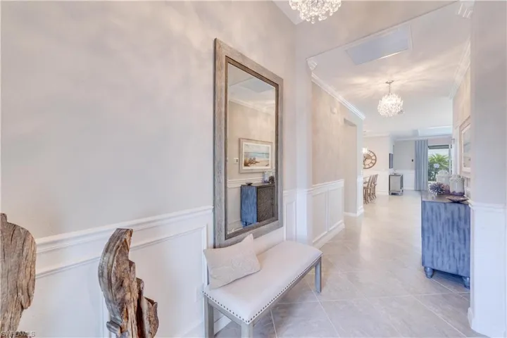 Hallway with a wainscoted wall, ornamental molding, visible vents, and a notable chandelier