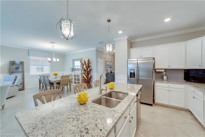Kitchen featuring a center island with sink, white cabinetry, stainless steel refrigerator with ice dispenser, and a stainless undermount sink and beautiful light fixtures
