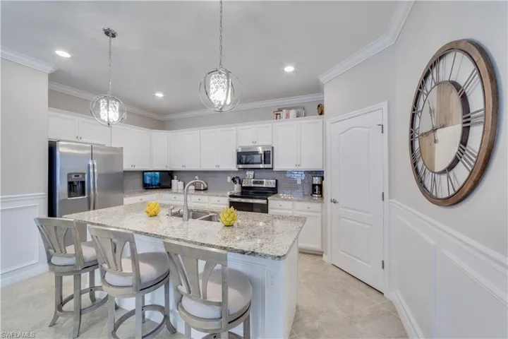 Kitchen with white cabinets, an island with sink, decorative light fixtures, and stainless steel appliances. Large kitchen pantry.