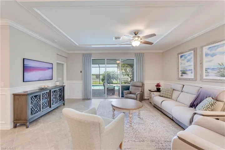Living area with ceiling fan, a decorative wall, a sunroom, and wainscoting. Enjoy the views and the large frame TV.