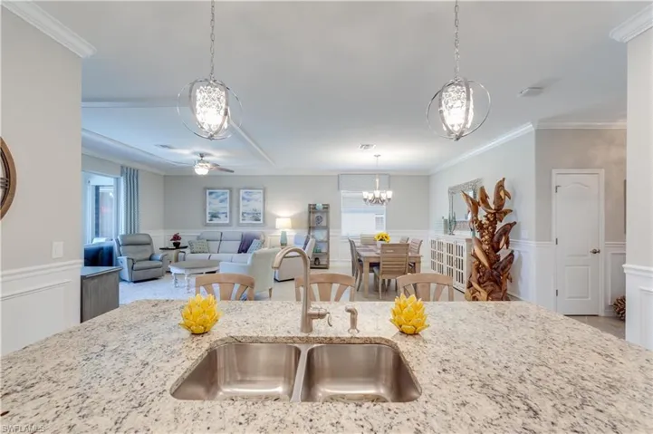 Kitchen with a wainscoted wall, a sink, open floor plan, light stone countertops, and crown molding