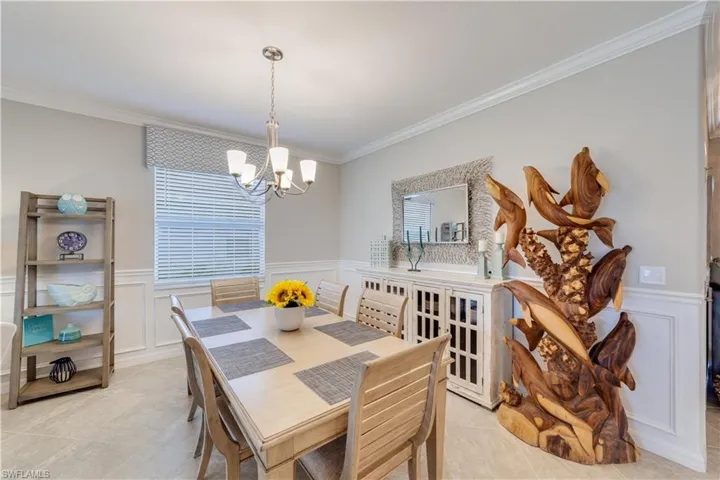 Dining room with light tile patterned flooring, ornamental molding, a chandelier, and wainscoting