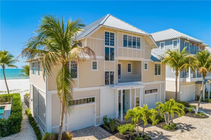 View of front of house featuring a balcony, an attached garage, driveway, view of water and beach, and board and batten siding