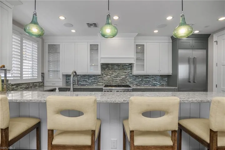 Kitchen featuring a breakfast bar area, decorative light fixtures, light stone counters, stainless steel appliances, and decorative backsplash