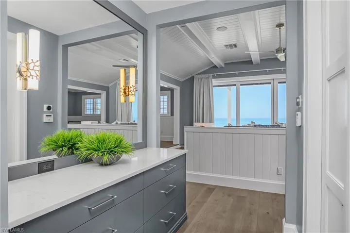 Bathroom with lofted ceiling with beams, dark wood-style floors, vanity, a ceiling fan, and a water view
