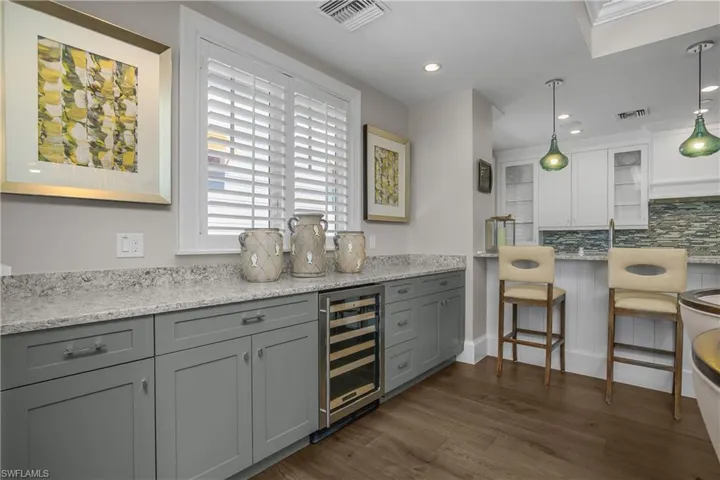 Bar featuring light stone counters, beverage cooler, dark wood-style flooring, and tasteful backsplash