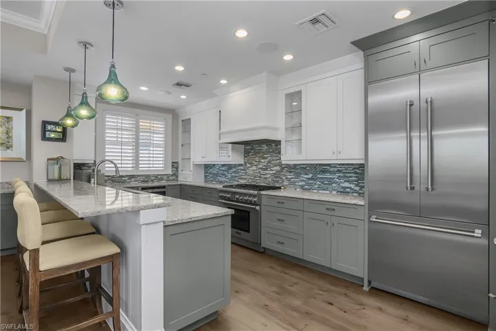 Two tone kitchen with premium appliances, decorative light fixtures, a peninsula, light stone counters, and tasteful backsplash