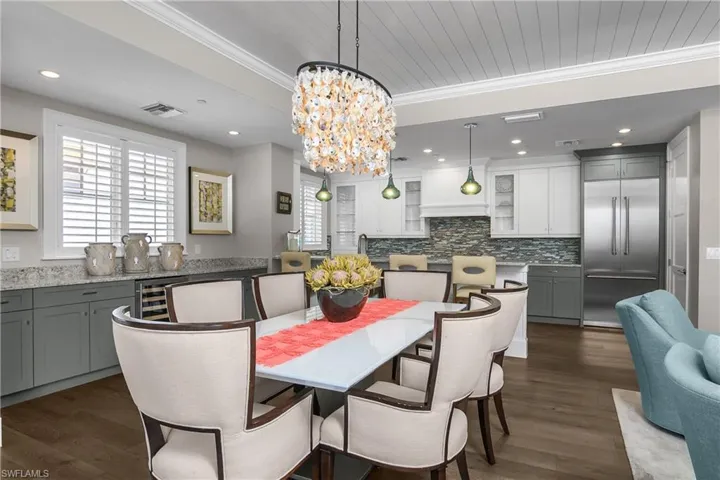 Dining space with ornamental molding, suspended lighting, dark wood-style floors, and beverage cooler