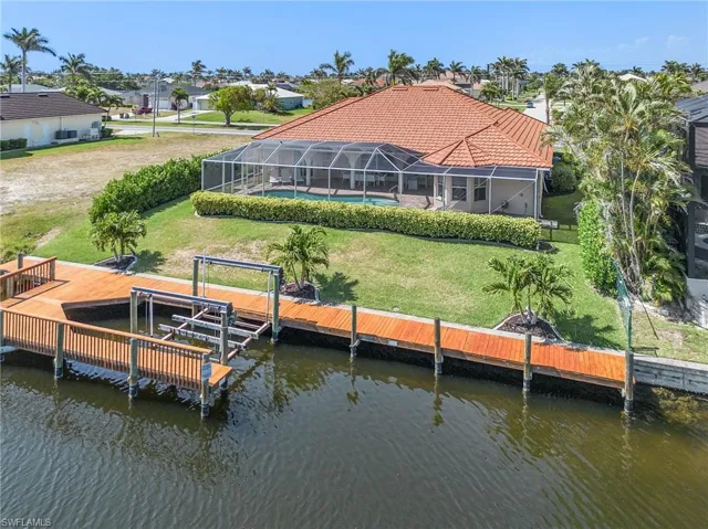 Back of house featuring a water view, boat lift, a tile roof, and an outdoor pool
