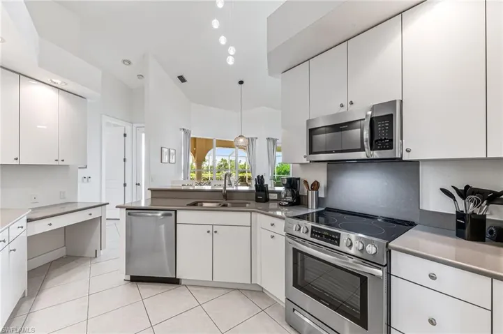 Kitchen with stainless steel appliances, white cabinets, light tile patterned floors, high vaulted ceiling, and light countertops