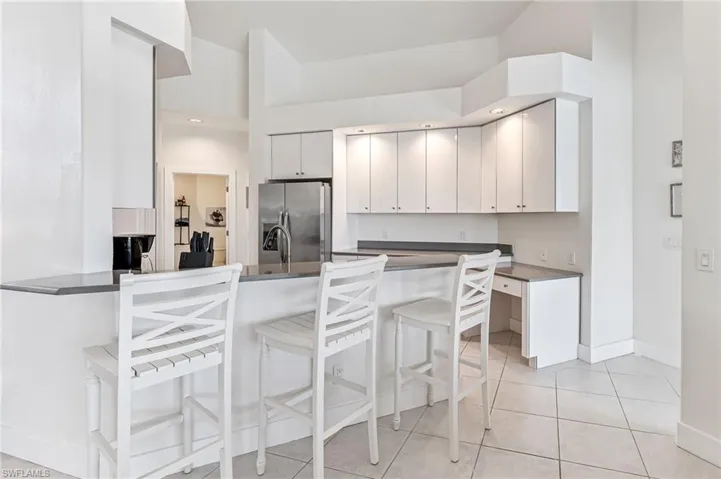 Kitchen with stainless steel appliances, a peninsula, white cabinetry, and light tile patterned floors