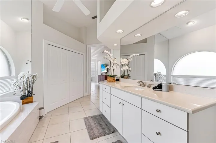 Full bath with vanity, a garden tub, a ceiling fan, tile patterned flooring, and high vaulted ceiling