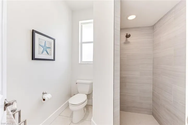 Bedroom with access to outside, a raised ceiling, ensuite bath, light tile patterned floors, and ceiling fan