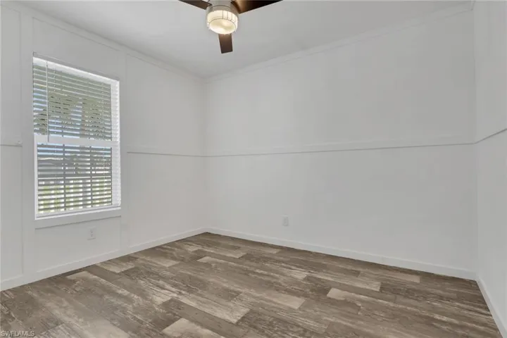 Interior space featuring wood-finish flooring, chair rail molding, a neutral color palette, and a ceiling fan with integrated lighting