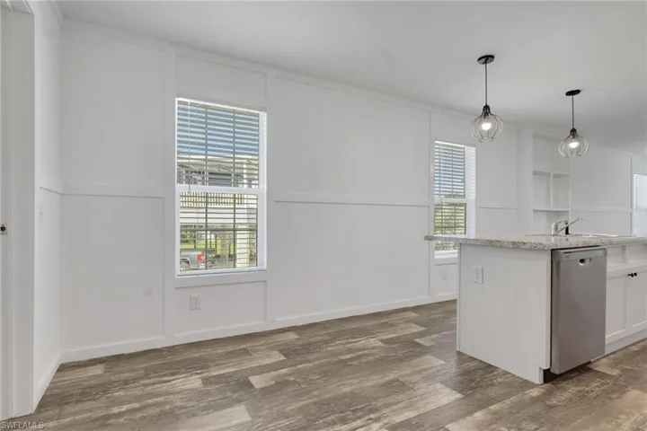 Interior space featuring board-and-batten wall detailing, wood-finish flooring, dual glass pendant light fixtures, and a kitchen island with a stone-surfaced countertop and stainless steel dishwasher