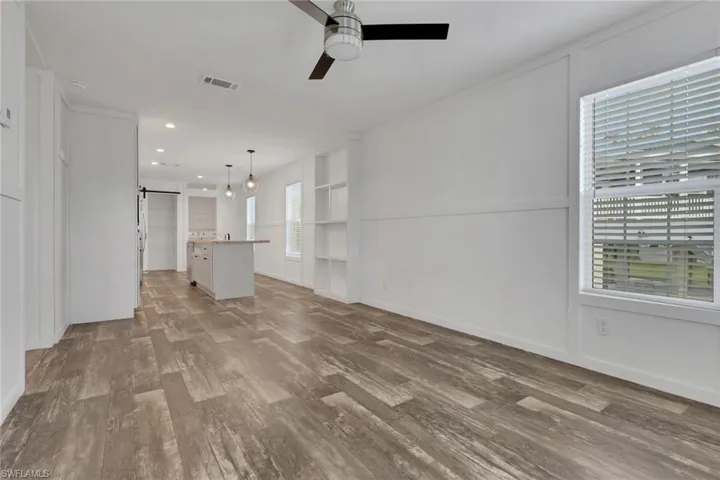 Wood-finish flooring, board and batten wainscoting, built-in shelving, ceiling fan with integrated lighting, and a central kitchen island