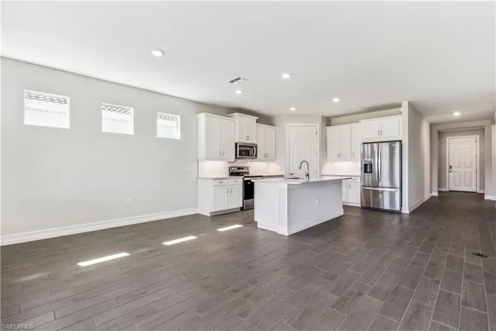Kitchen featuring dark hardwood / wood-style floors, a healthy amount of sunlight, appliances with stainless steel finishes, and an island with sink