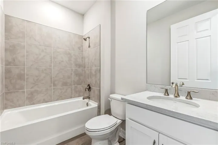 Full bathroom featuring vanity, tiled shower / bath, hardwood / wood-style flooring, and toilet