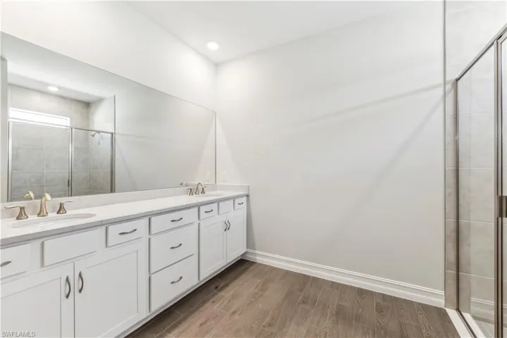 Bathroom with a shower with shower door, hardwood / wood-style flooring, and double vanity