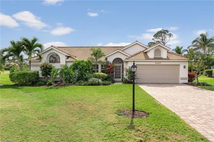 View of front of property featuring an attached garage, a tile roof, decorative driveway, stucco siding, and a front lawn