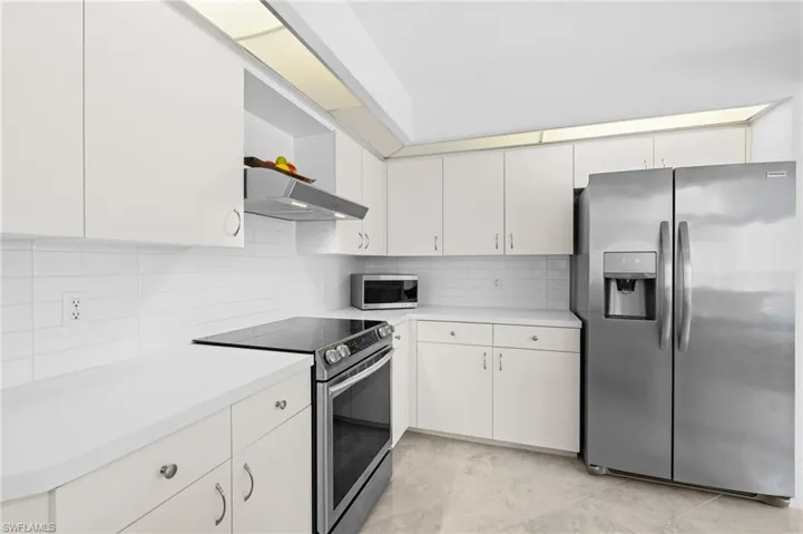 Kitchen with stainless steel appliances, light countertops, decorative backsplash, white cabinetry, and under cabinet range hood