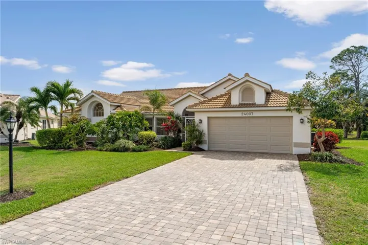 View of front facade featuring a tile roof, an attached garage, decorative driveway, a front lawn, and stucco siding