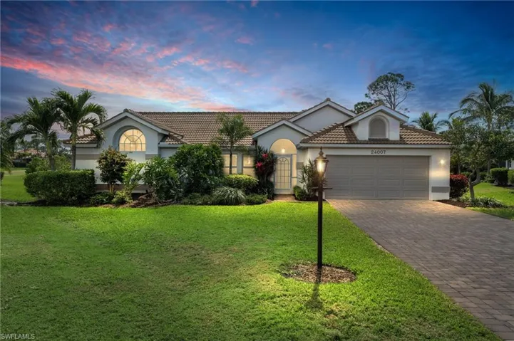 Single story home with a garage, a tile roof, decorative driveway, a lawn, and stucco siding
