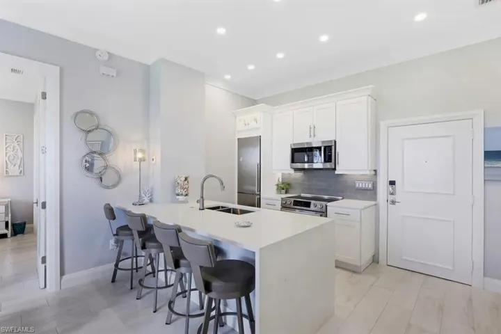 Kitchen with white cabinets, stainless steel appliances, backsplash, a sink, and a breakfast bar area