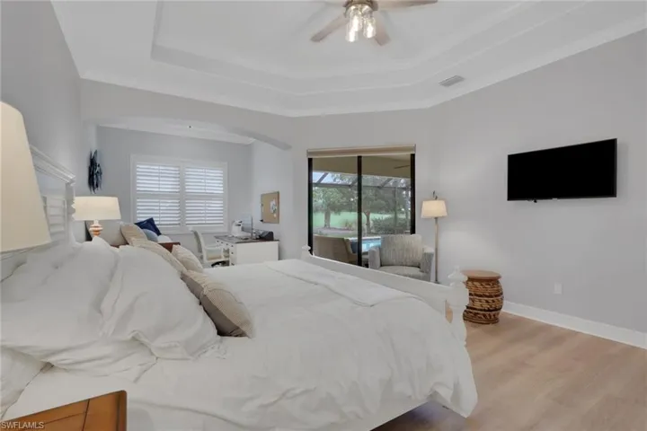 Bedroom with access to exterior, ornamental molding, wood finished floors, a ceiling fan, and a raised ceiling