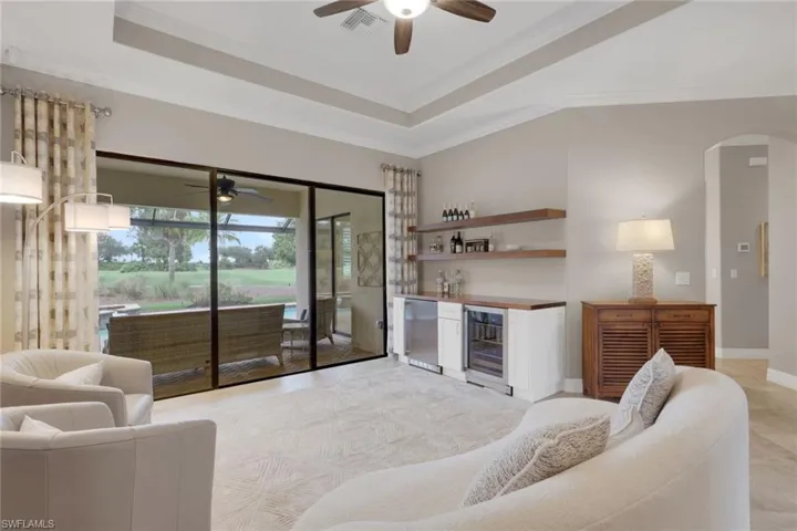 Living area featuring a bar, beverage cooler, a ceiling fan, arched walkways, and ornamental molding