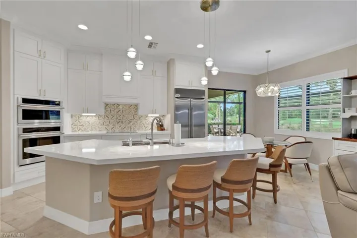 Kitchen with backsplash, white cabinetry, a breakfast bar, an island with sink, and light stone countertops