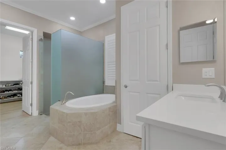 Bathroom with a garden tub, vanity, crown molding, light tile patterned floors, and recessed lighting