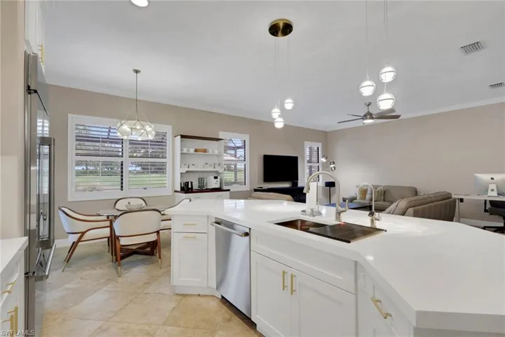 Kitchen with white cabinetry, open floor plan, decorative light fixtures, stainless steel appliances, and ornamental molding