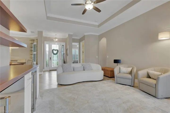 Living area featuring a tray ceiling, light tile patterned floors, beverage cooler, a ceiling fan, and crown molding
