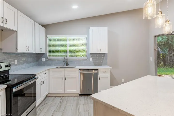Kitchen featuring appliances with stainless steel finishes, lofted ceiling, decorative backsplash, light stone counters, and white cabinetry