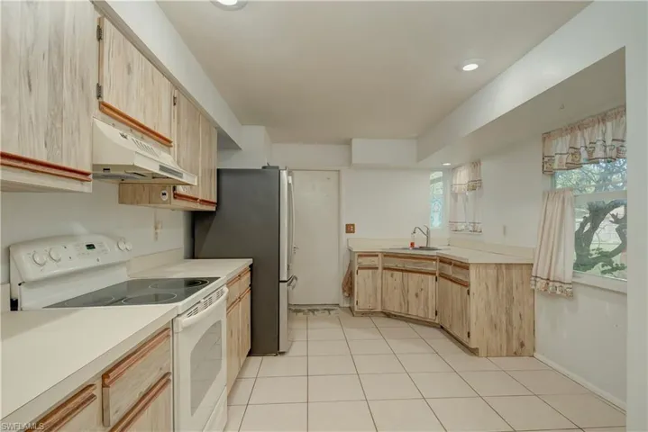 Kitchen featuring light brown cabinetry, white range with electric stovetop, under cabinet range hood, light countertops, and recessed lighting