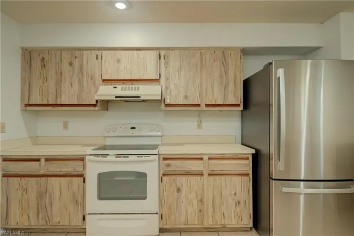 Kitchen with light brown cabinets, freestanding refrigerator, electric stove, light countertops, and light tile patterned flooring