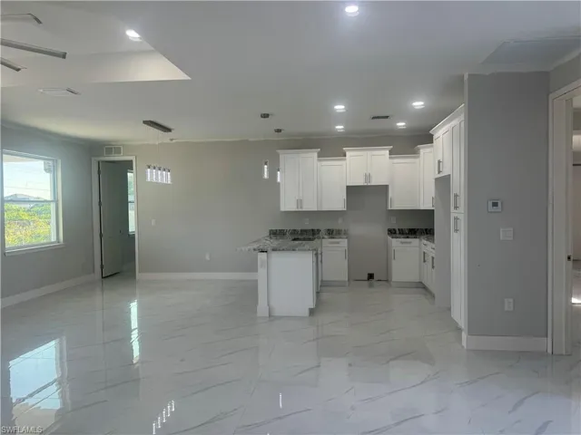 Kitchen with dark stone counters, a kitchen island, light tile floors, hanging light fixtures, and white cabinets