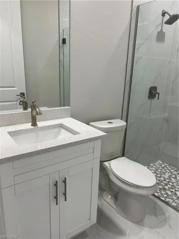 Bathroom with a shower with shower door, tile flooring, vanity, and toilet